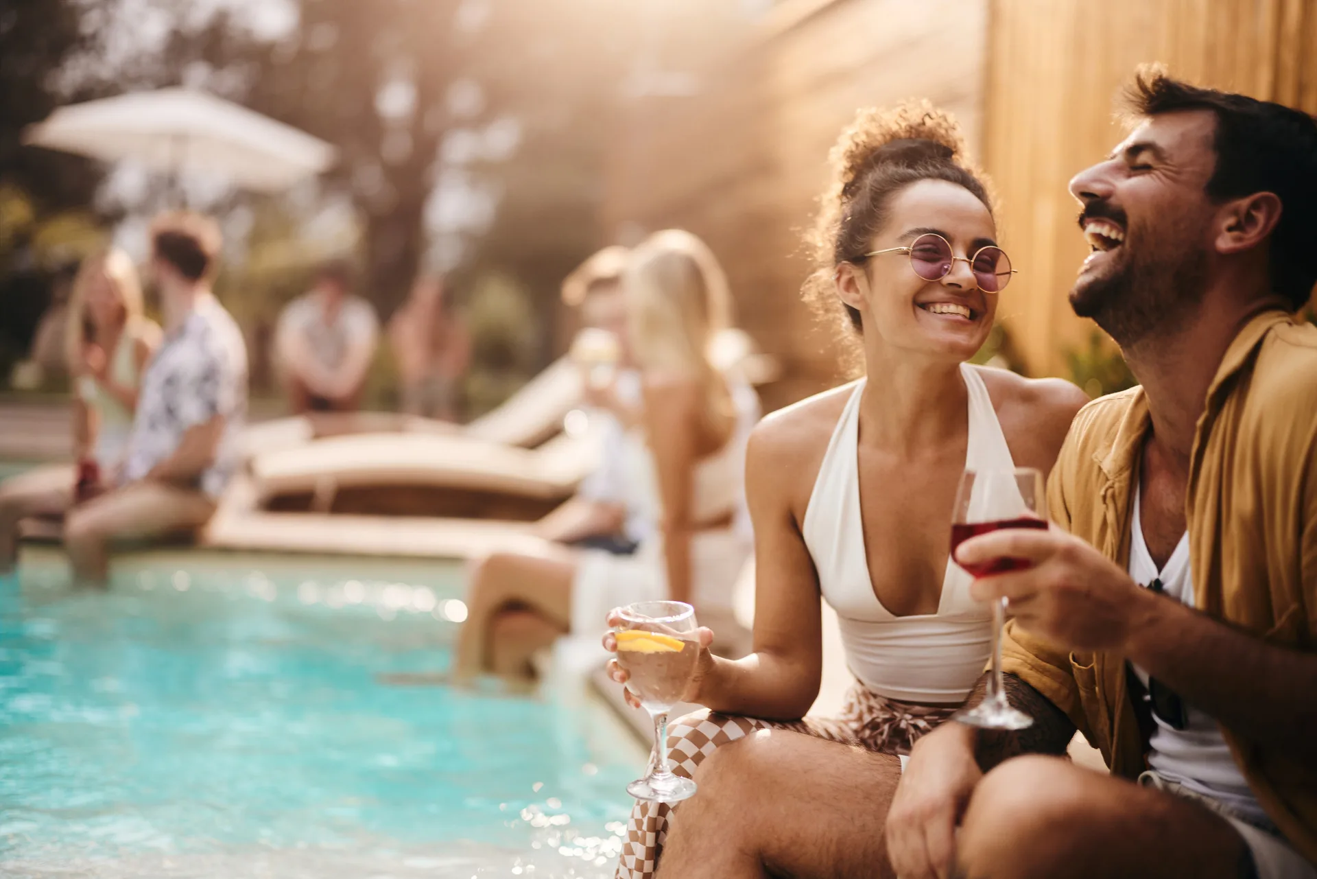 Young cheerful couple enjoying in conversation and drinks during a pool party with their friends.